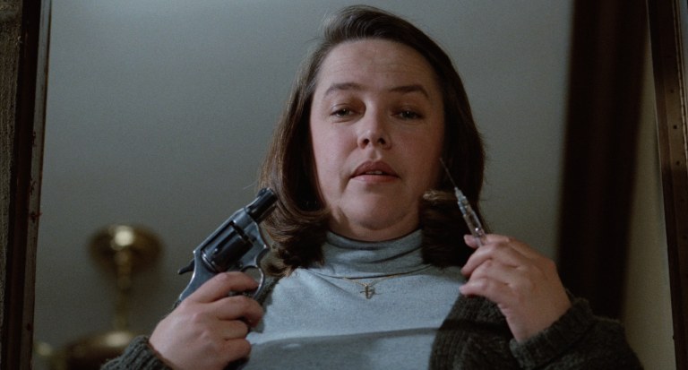 Kathy Bates holds a gun and a syringe in Misery (1990).