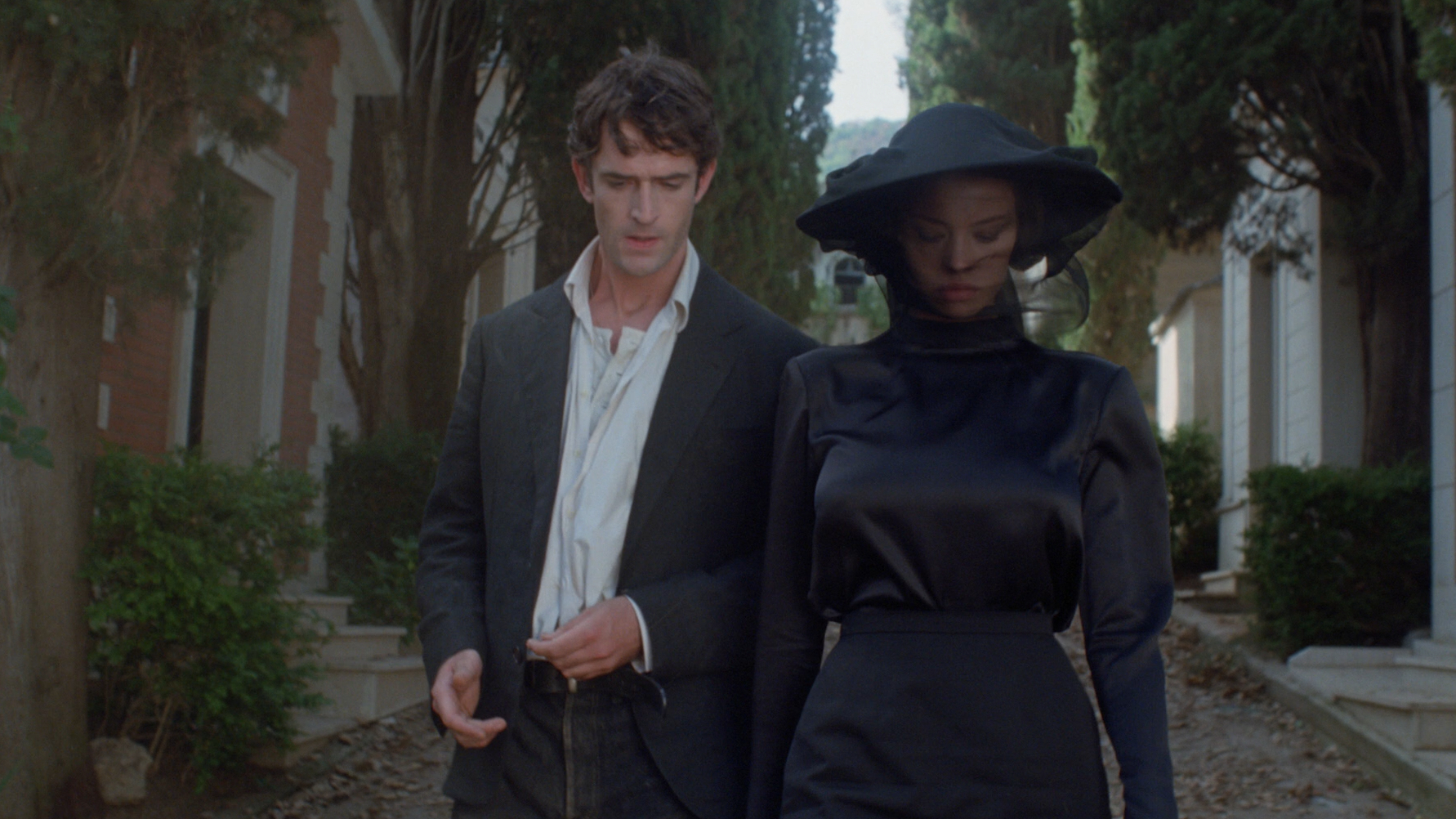 Rupert Everett and Anna Falchi walk down a path in a cemetery in Cemetery Man (1994).