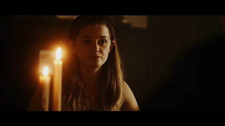 Alice sits at a table with two candles in Alice in Terrorland.