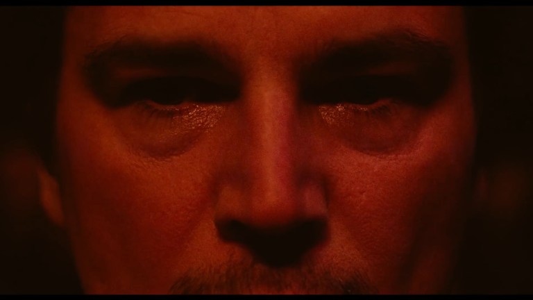 Josh Hartnett stares at us through a red light in Trap (2024).