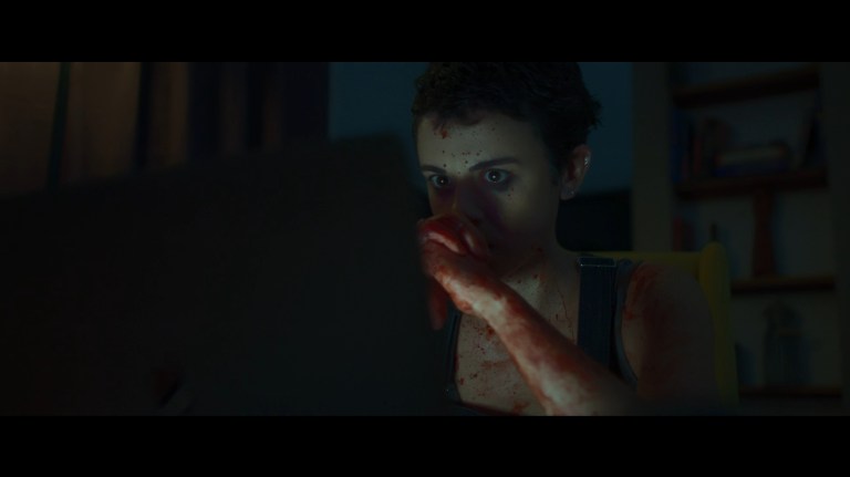 Bowie, splattered with blood, looks at her laptop in Faceless After Dark (2023).