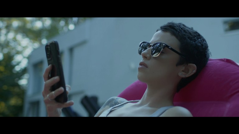 Bowie scrolls through her phone while floating in a swimming pool in Faceless After Dark (2023).