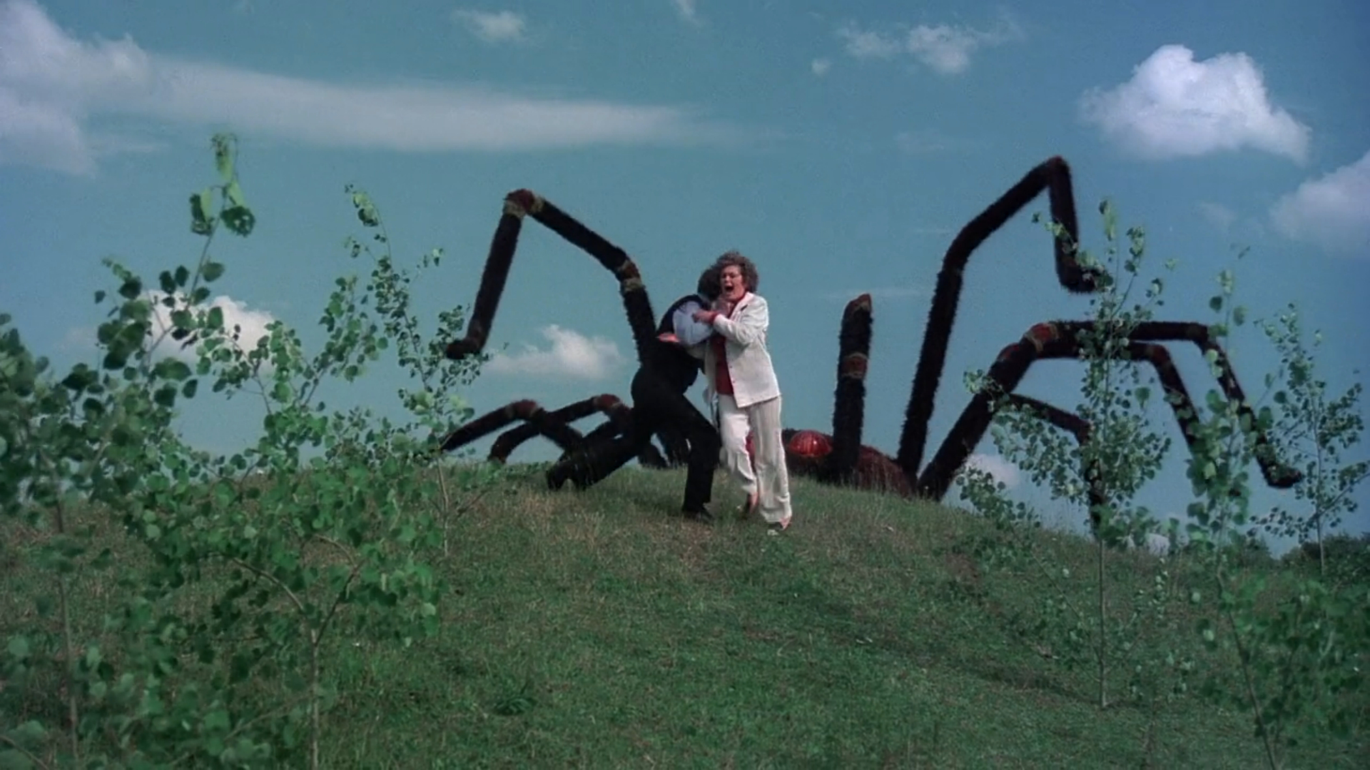 A giant spider scares two people as it rises over a hill in The Giant Spider Invasion (1975).