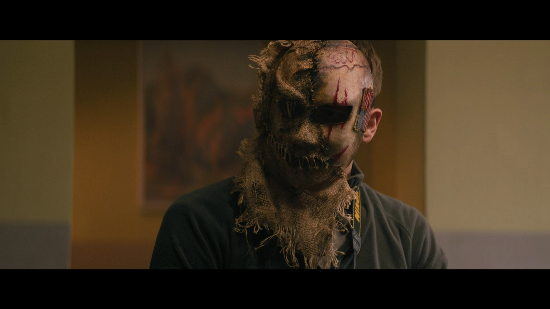 A man wearing a burlap mask in Refuge (2023).