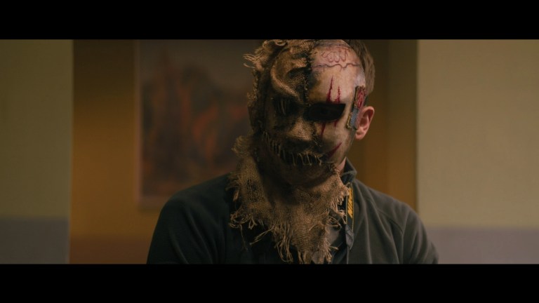 A man wearing a burlap mask in Refuge (2023).