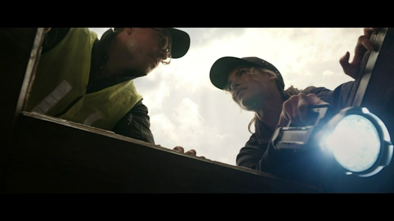 Michael and Elena talk to each other while crouching above a hatch in the ship in Ship of the Damned (2024).