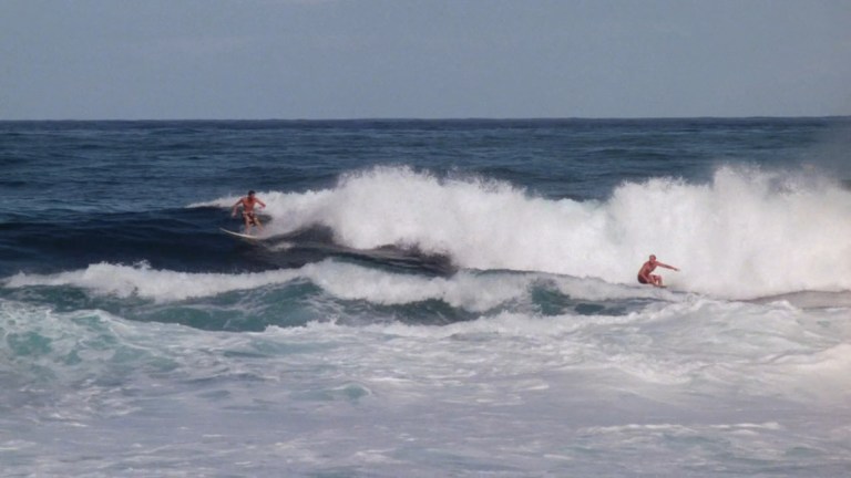 Two men surf in Blood Surf (2000).