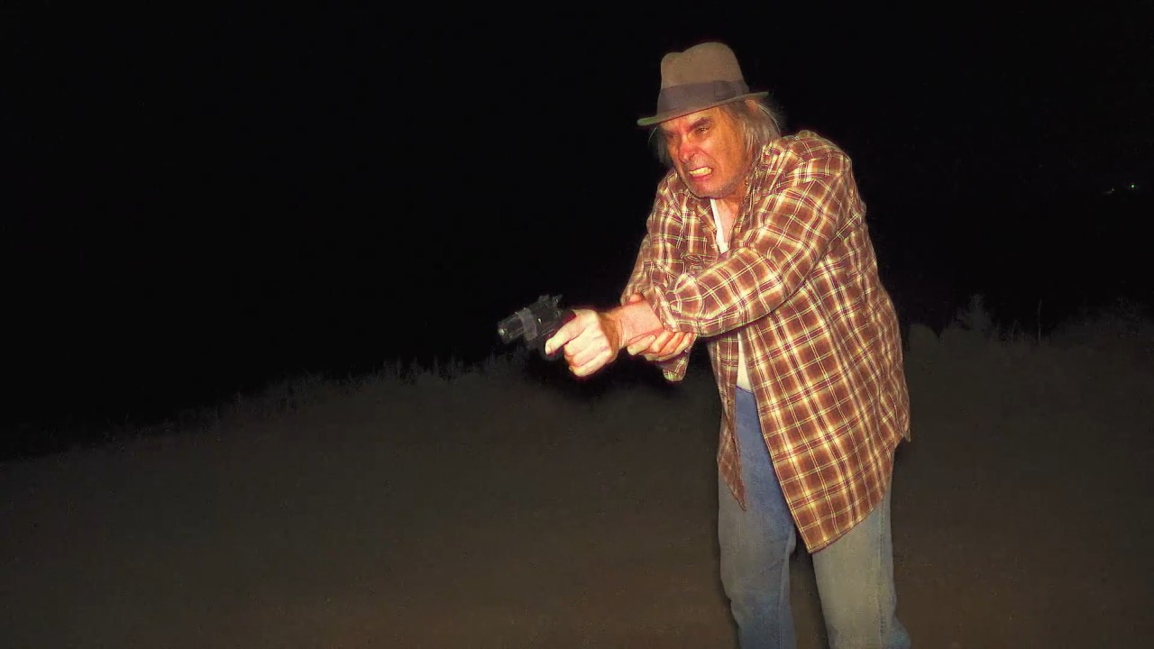 Greg holds a gun in Milk & Serial (2024).