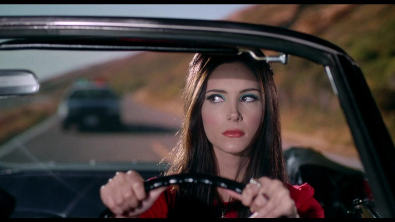 Elaine spots a police car behind her in The Love Witch (2016).