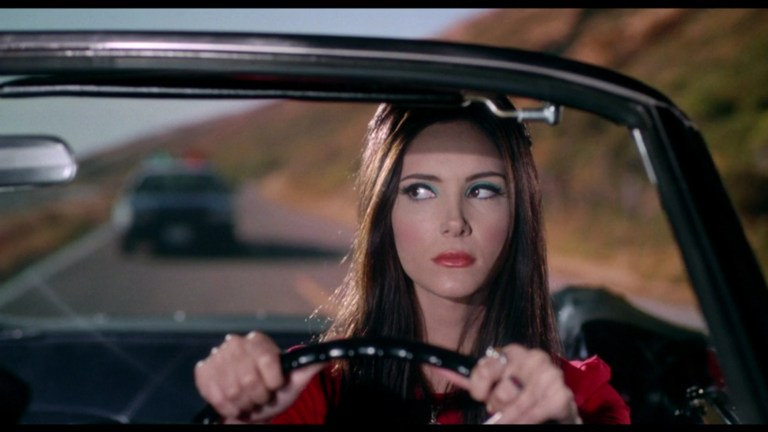 Elaine spots a police car behind her in The Love Witch (2016).
