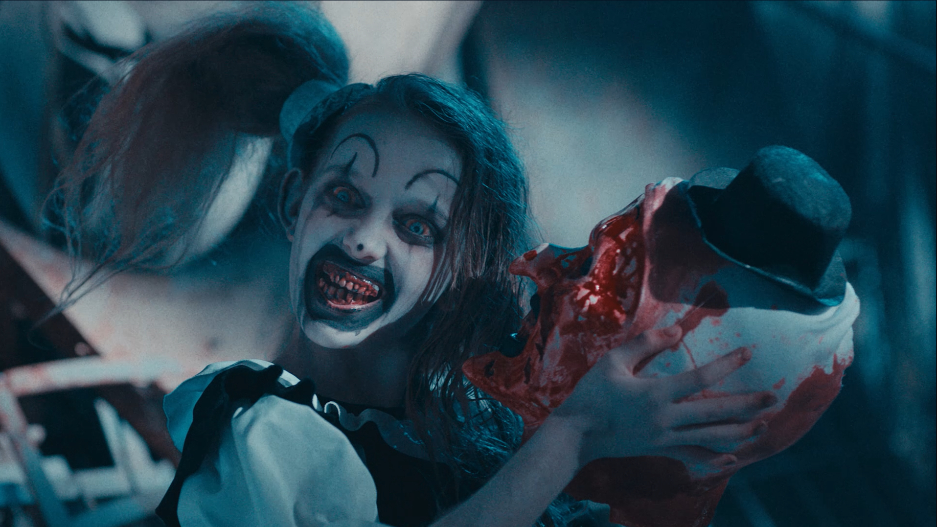 The Pale Girl smiles while holding Art the Clown's head in Terrifier 2 (2022).