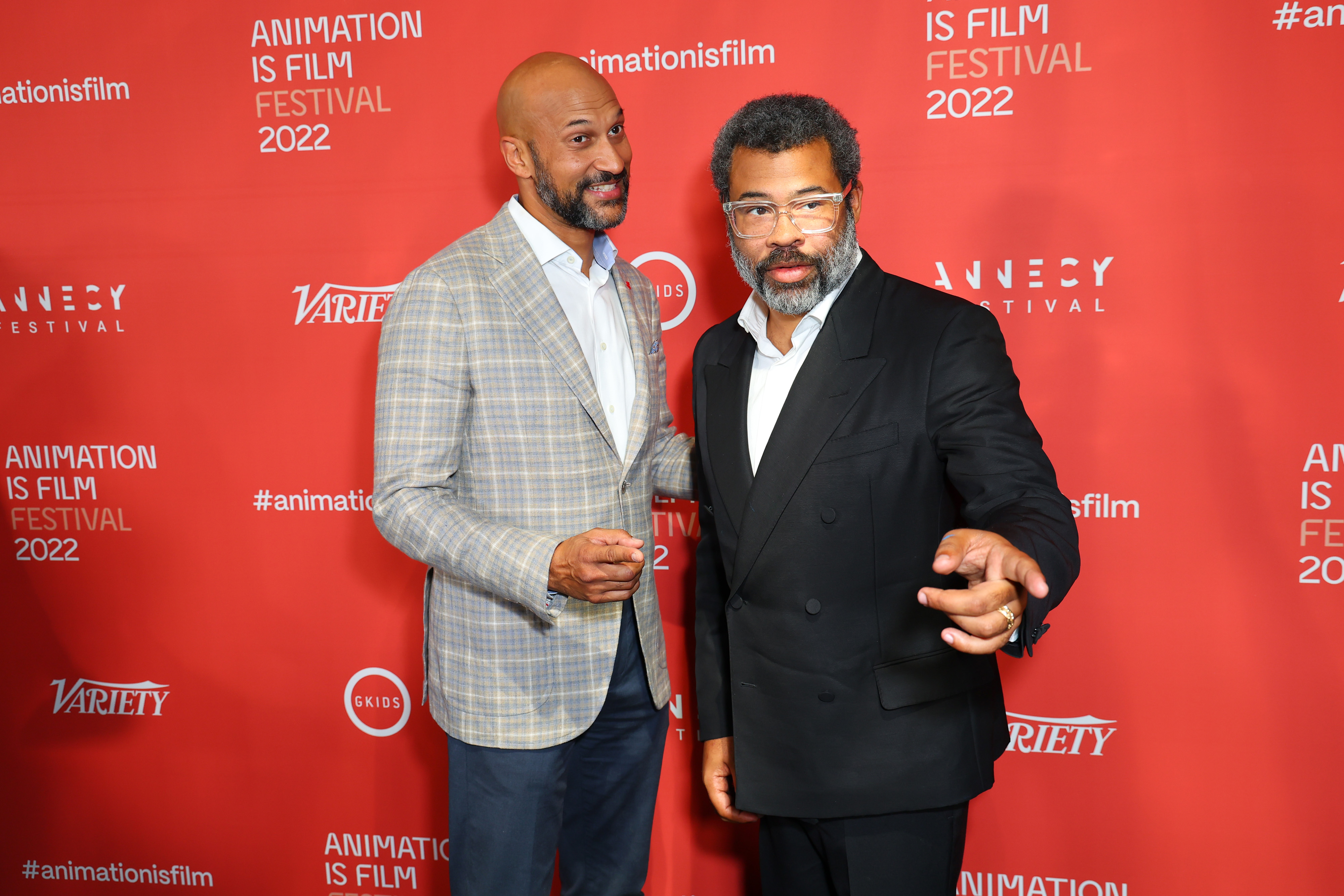Two men in suits standing in front of an Animation Is Film Festival 2022 step-and-repeat backdrop, one bald in a plaid blazer and the other in glasses and a black suit.